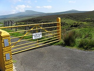 A fence blocking a small country road from movement of horses and cows.